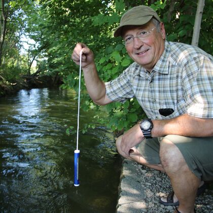 Kursleiter Gerhard Wurm sitzt an einem Bach und demonstriert eine spezielle Angeltechnik.